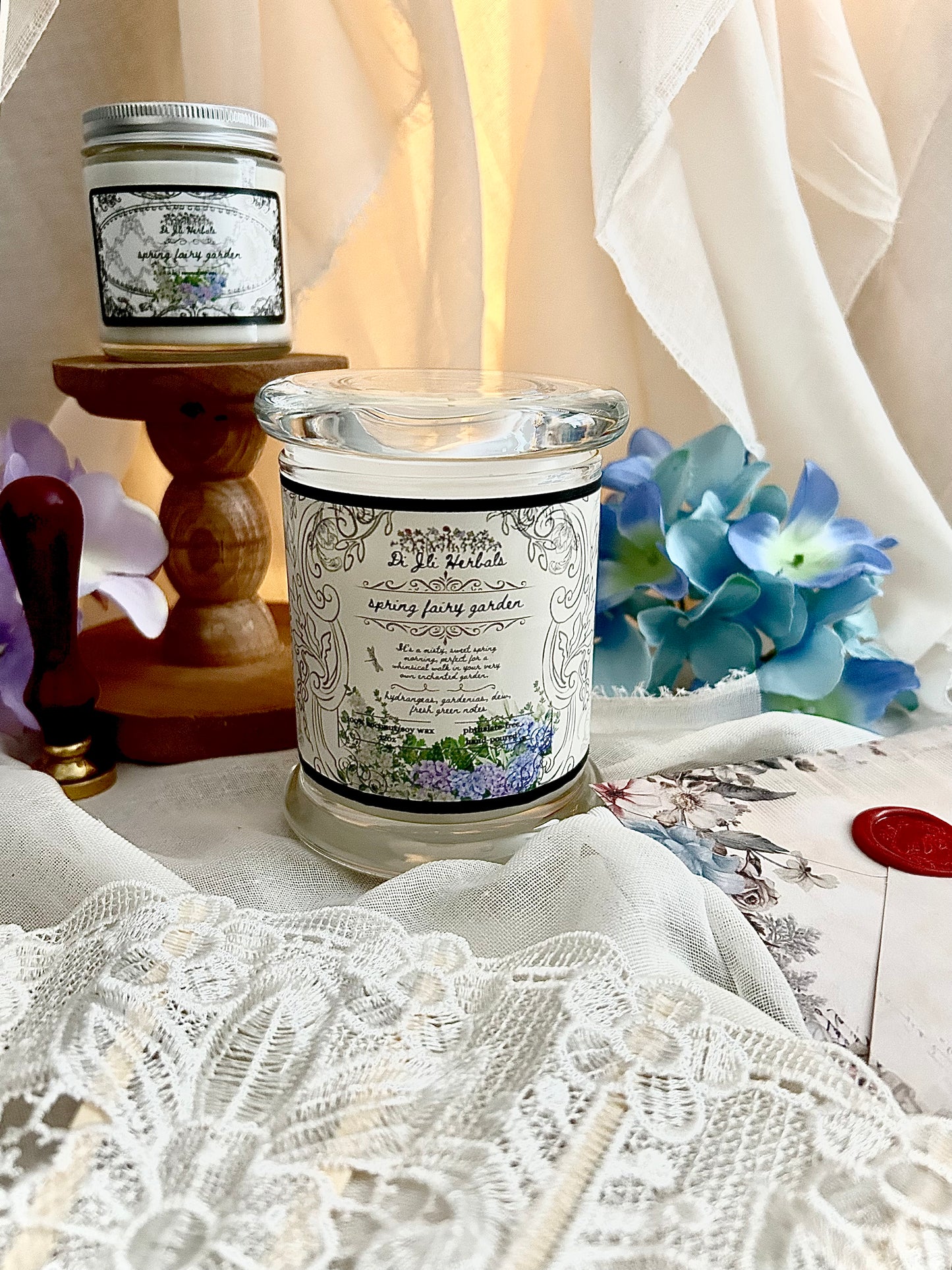 Hand-poured Victorian romantic-inspired candle with elegantly designed spring fairy garden label, in front of gardenias on a white lace tablecloth