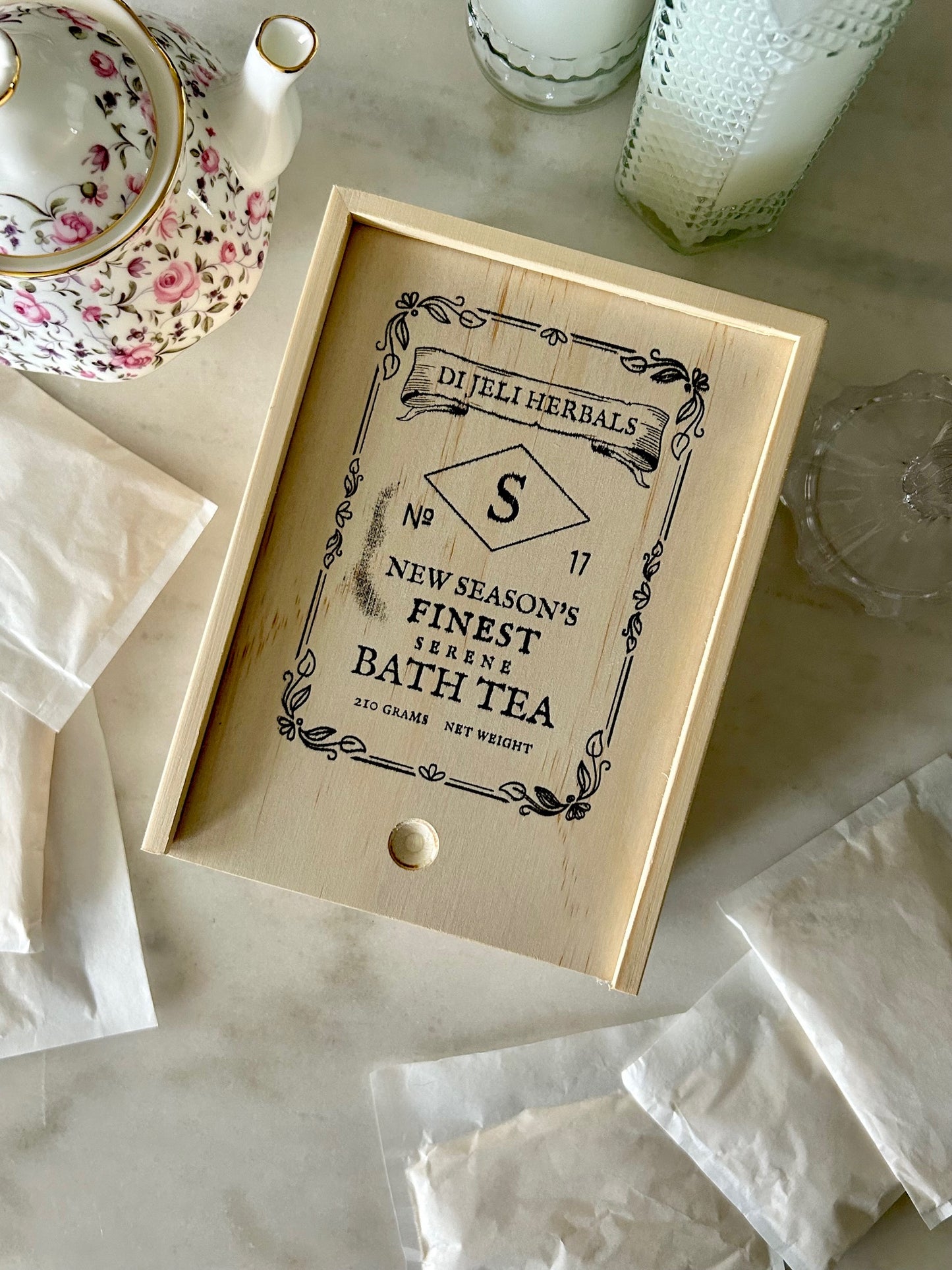 Small wooden box labeled 'New Season's Finest' with bath tea sachets on a marble surface.